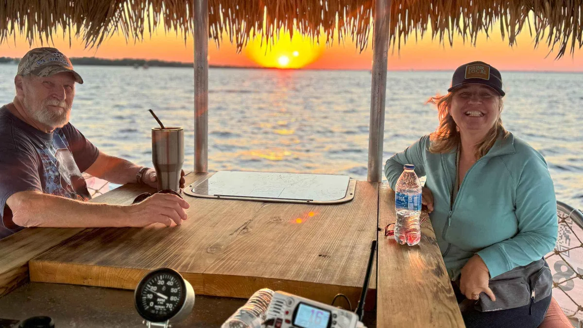 A tiki boat with guests under an orange sunset sky on a Shell Island dolphin tour from Panama City Beach, Florida